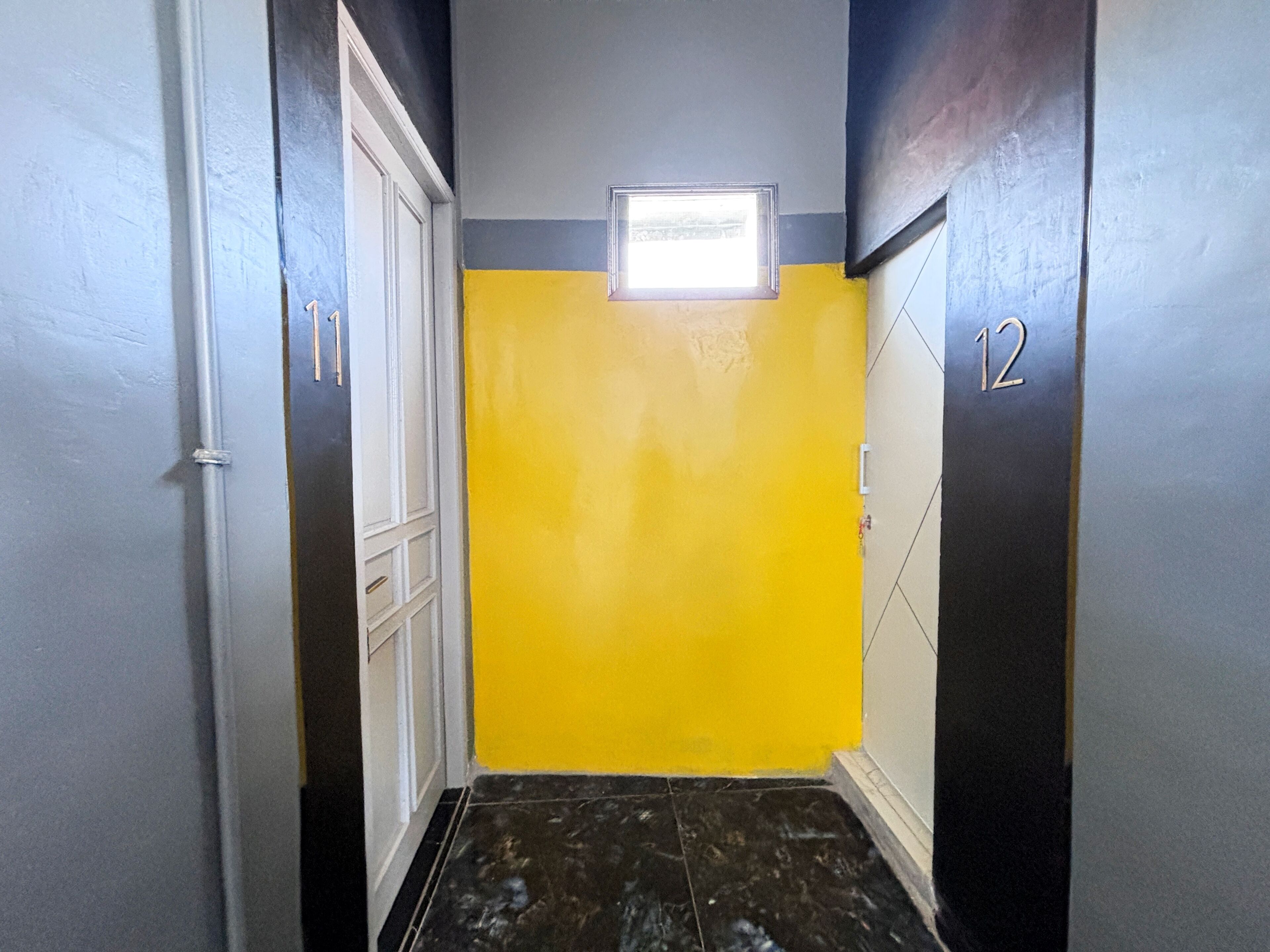 A hallway with a yellow wall, a small window, and a door marked with the number 12.