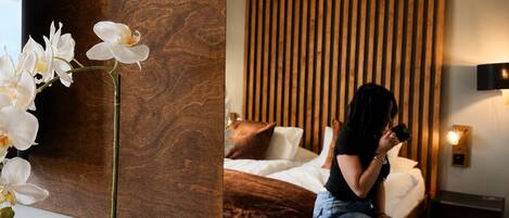 A modern bedroom with a wooden accent wall, a bed with a brown headboard, and a potted orchid on a wooden table.