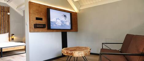A modern room with a wooden floor, a mounted TV, a wooden side table, and a brown leather chair.