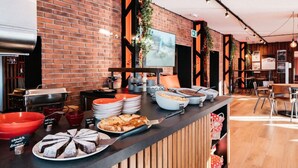 A buffet area with a brick wall, a television screen, and various food items. - Alaia Lodge (Crans-Montana)