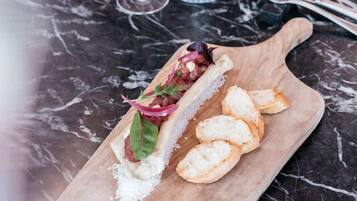 A dining table with a wooden serving board holding a sandwich and bread slices, a wine glass, and a water glass.