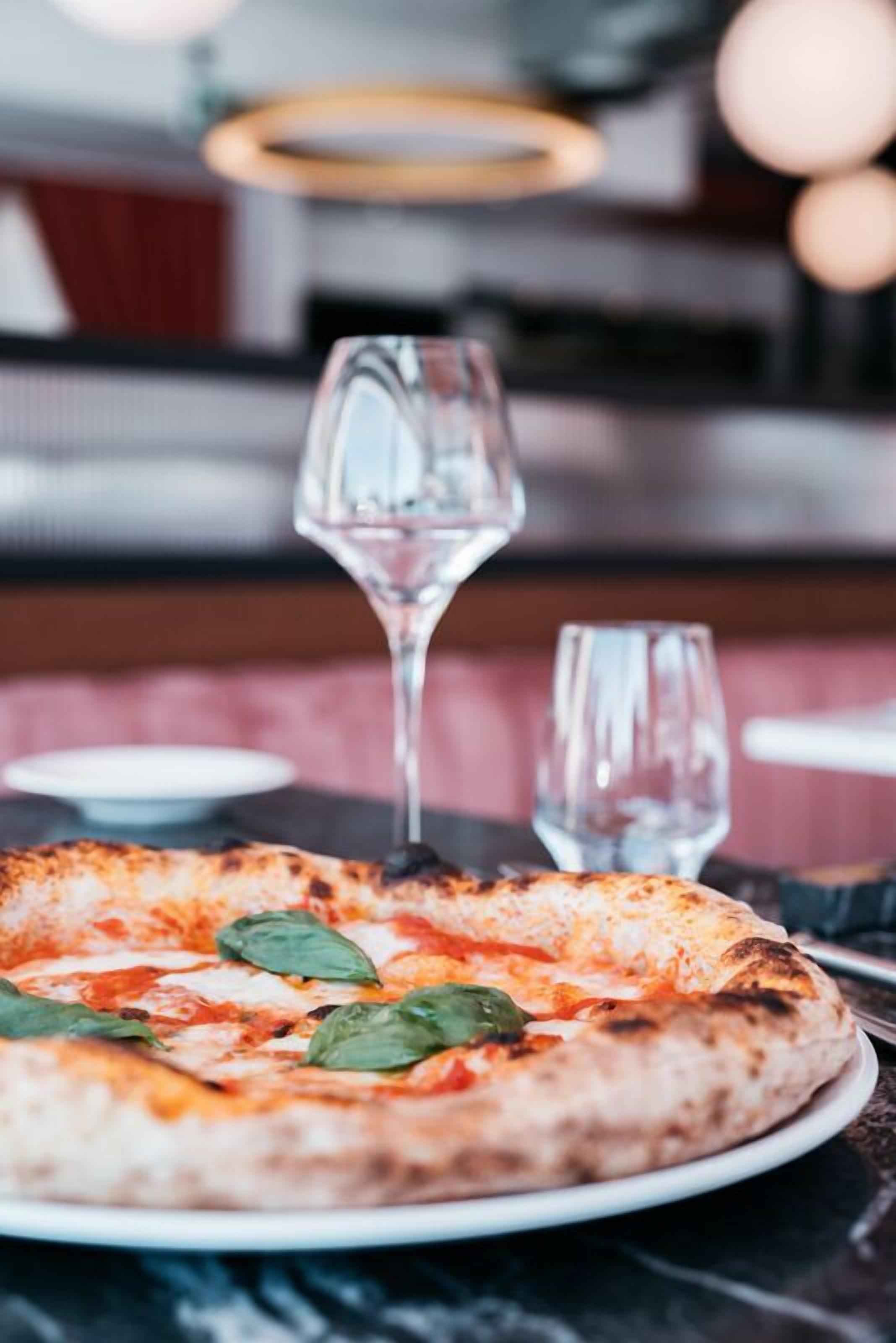 Pizza op een bord, met een glas water en een wijnglas op de achtergrond.
