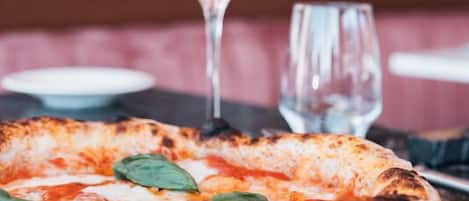 A pizza on a plate with a glass of water and a wine glass in the background.