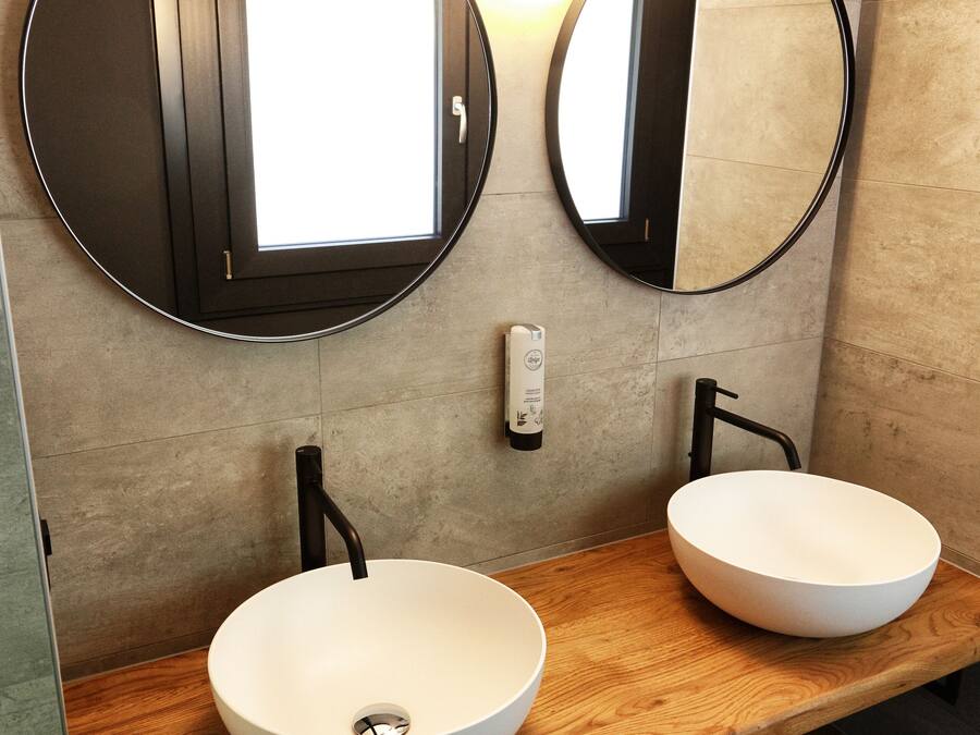 Une salle de bain avec deux miroirs ronds, un meuble-lavabo en bois et un luminaire fixé au mur.