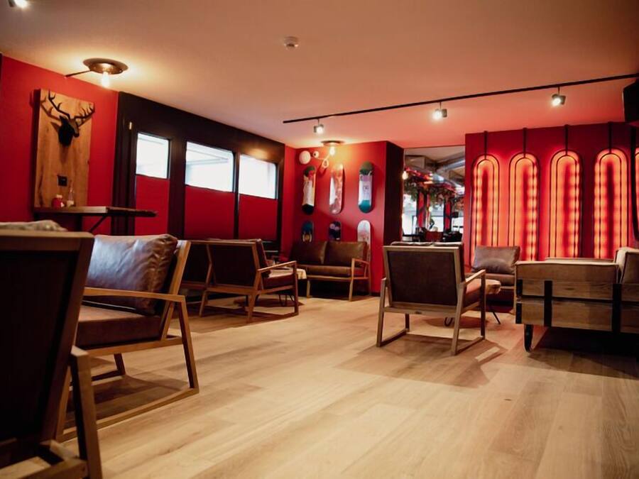 A modern interior with wooden flooring, red walls, and a variety of seating options including chairs and a sofa.