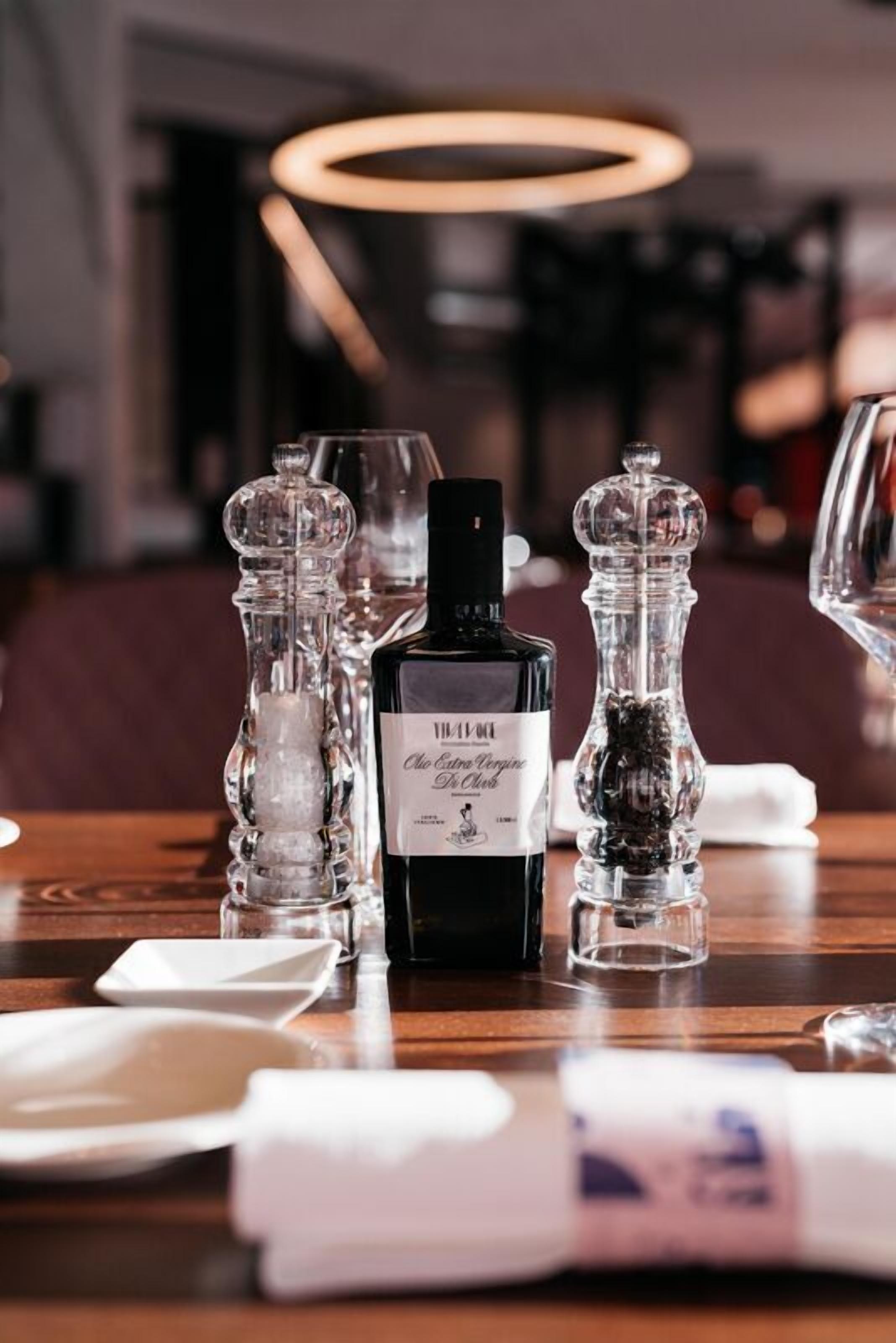 Una mesa servida con una botella de licor, saleros y pimenteros, y vasos.