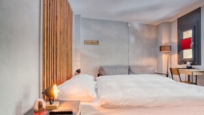 A modern hotel room with a bed, bedside table, lamp, and a desk with a chair. - Alaia Lodge (Crans-Montana)