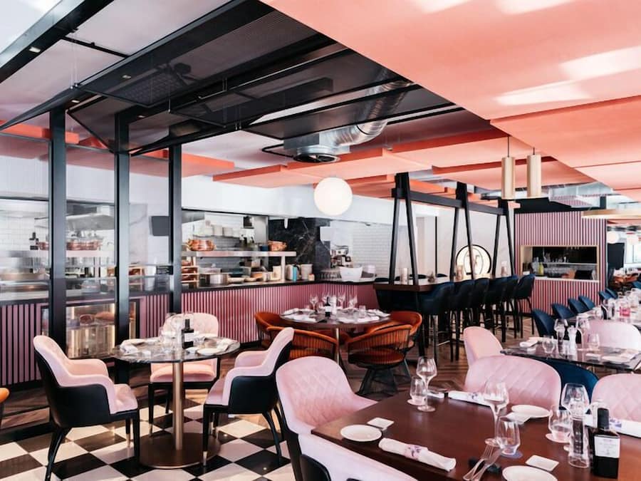 Un restaurante con piso a cuadros, sillas tapizadas en rosa y una zona de bar con taburetes.