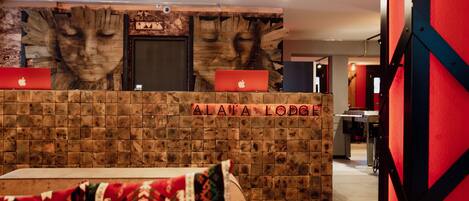 A reception desk with a wooden backdrop and a laptop, labeled "ALAVA LODGE".