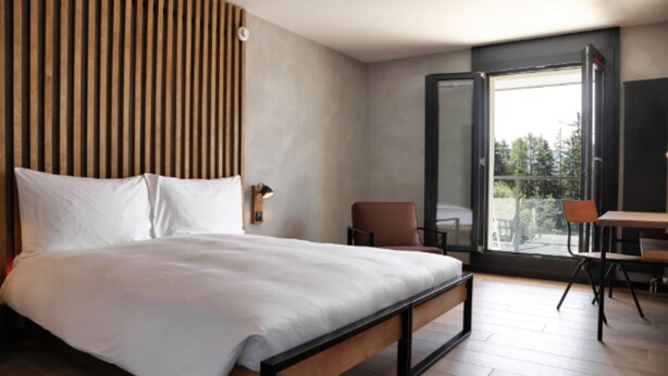 A modern bedroom with a wooden headboard, a large bed, a small table, and a chair. - Alaia Lodge (Crans-Montana)