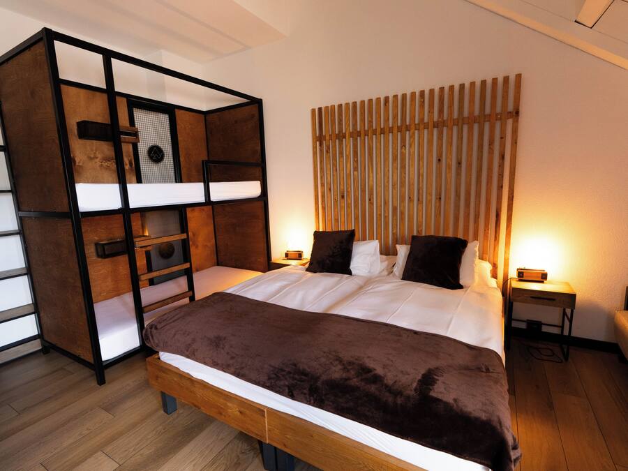 Un dormitorio con una cama individual superpuesta, una mesita de noche con lámpara y un cabecero de madera.