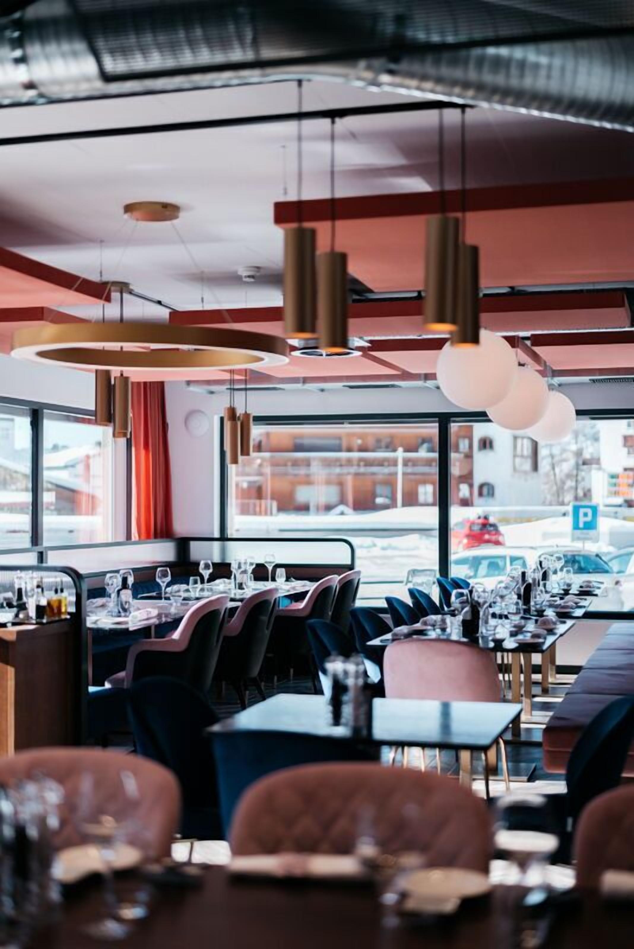 A restaurant with a long dining table, multiple chairs, and hanging pendant lights.