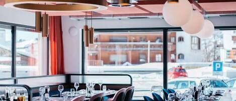 A restaurant with a long dining table, multiple chairs, and hanging pendant lights.