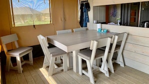Una mesa de comedor de madera con seis sillas, una ventana con vistas a la vegetación y una pared de madera con un perchero.