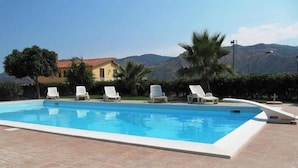 A swimming pool with white lounge chairs, a tiled deck, and a mountain backdrop. - Agriturismo Ghiritina (Francavilla di Sicilia)