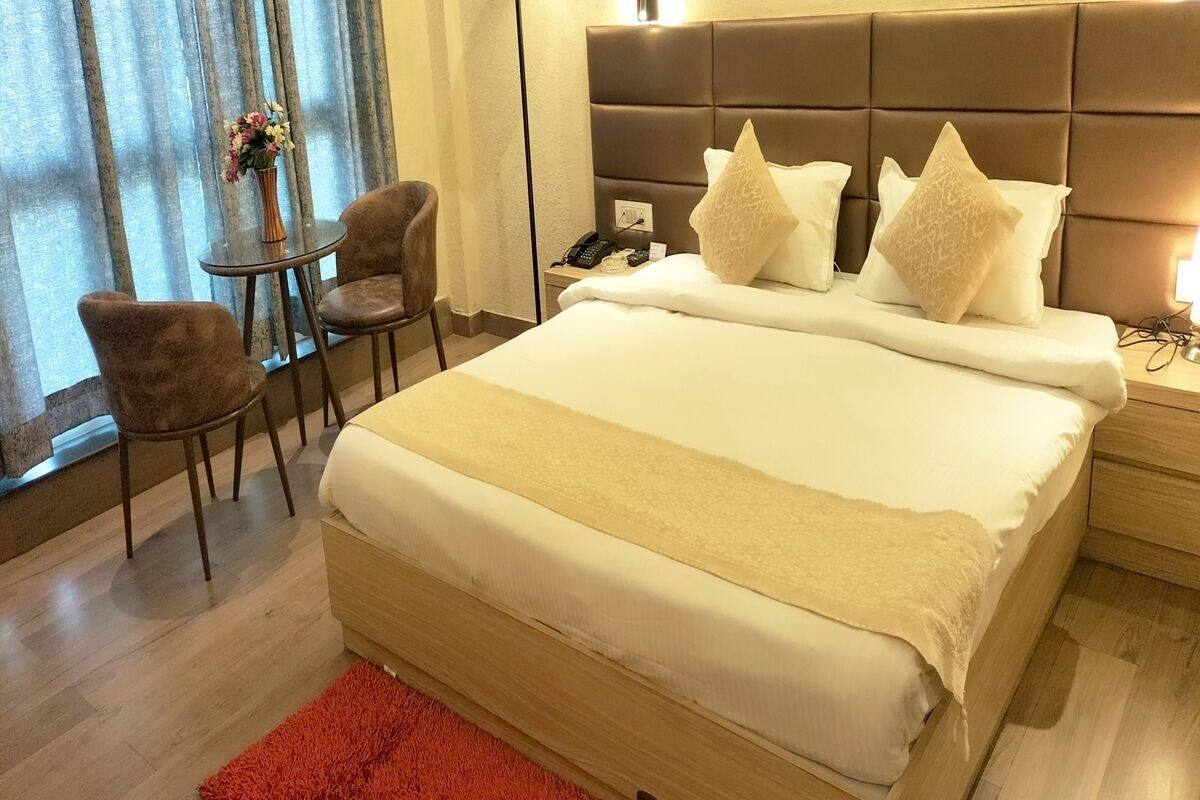 Une chambre d’hôtel avec un grand lit, une table de chevet avec un téléphone, une chaise et une petite table sur laquelle est posé un vase de fleurs.