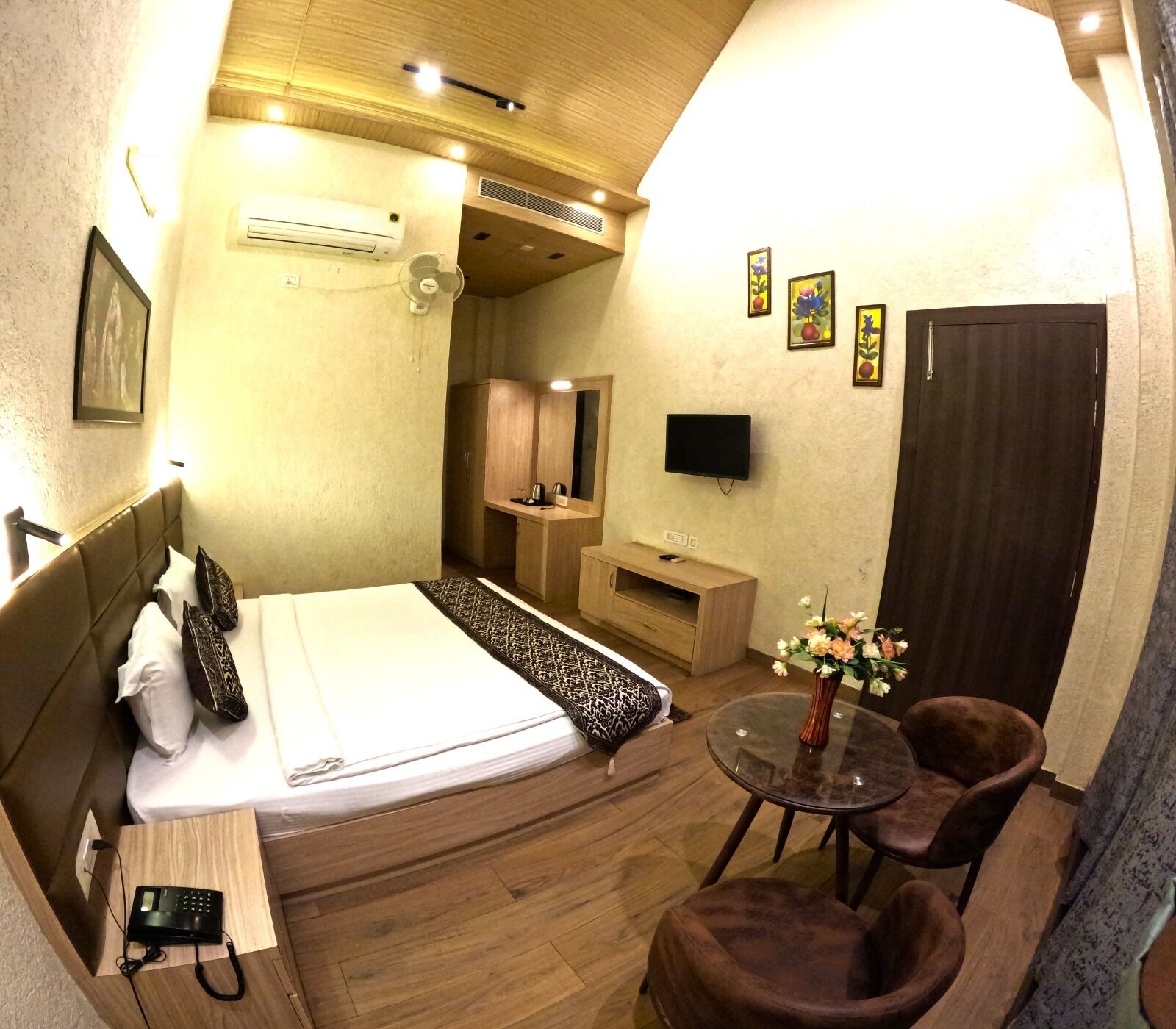 A hotel room with a bed, bedside table, chair, TV, and a small table with flowers.