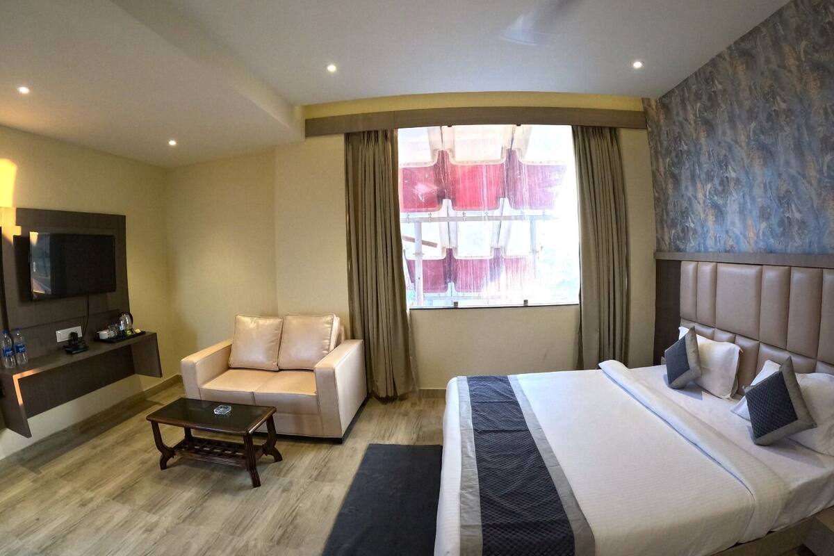 Une chambre d’hôtel avec un lit, un canapé, une table basse, une télévision et une fenêtre avec des rideaux.