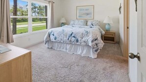 A bedroom with a bed, two bedside tables, a ceiling fan, a window with curtains, and a door. - 2BR Marco Island condo with pool, WiFi, and walk-to-beach access. (Marco Island)