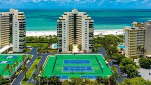 A high-rise hotel with multiple floors, a tennis court, and a beach view. - Beachfront 2BR/2BA Sandcastle condo with pool, WiFi, and heated pool (Marco Island)