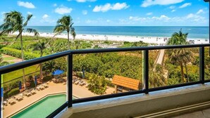 A balcony with a view of a beach, pool, and palm trees. - Beachfront 2BR/2BA Sandcastle condo with pool, WiFi, and heated pool (Marco Island)