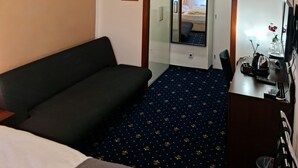 Habitación de hotel con cama, escritorio con computadora, silla, espejo y una mesita de noche con lámpara.