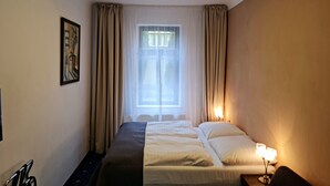 Habitación de hotel con cama, mesita de noche con lámpara, ventana con cortinas y un cuadro en la pared.