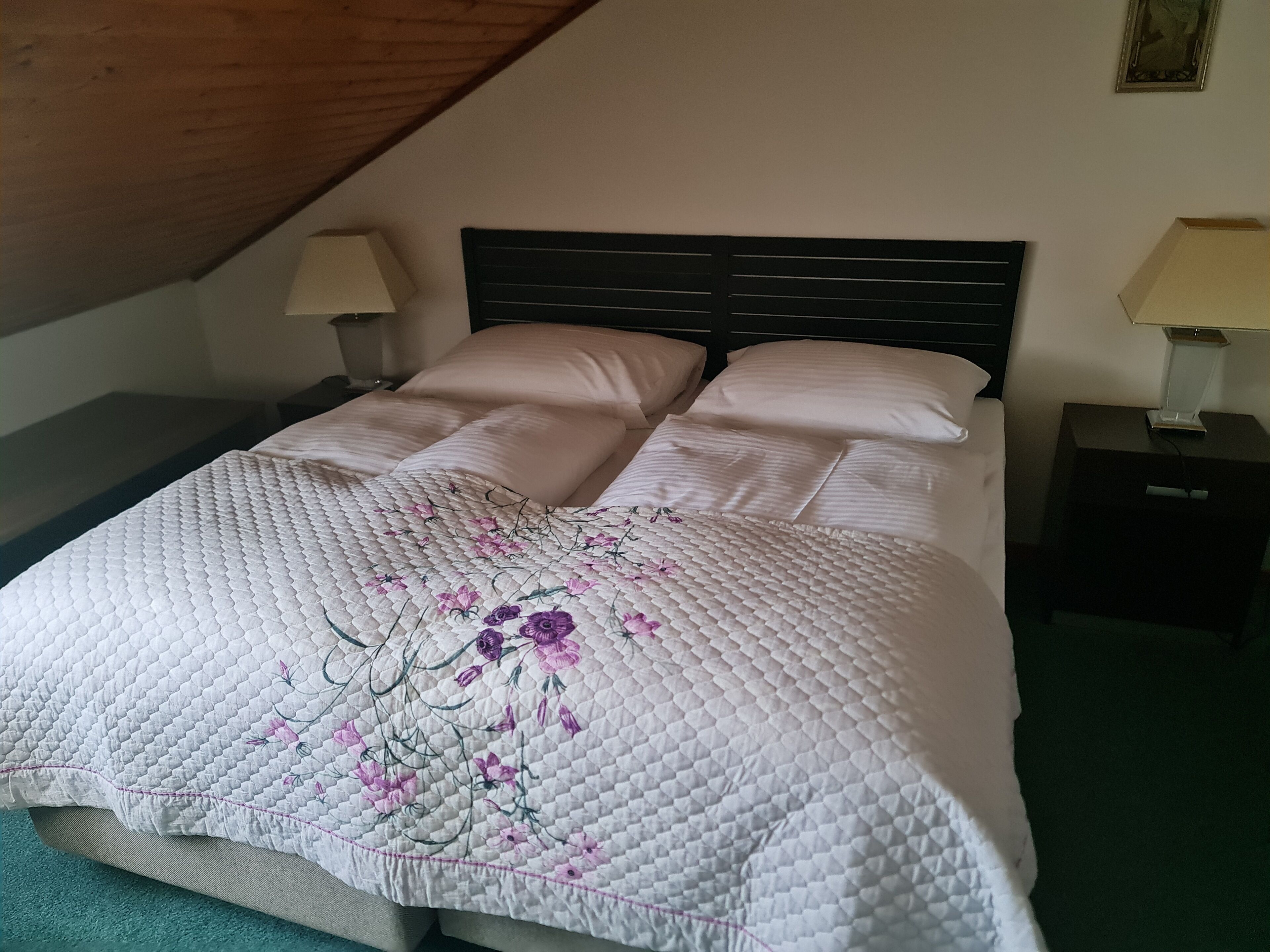 A neatly made bed with a floral quilt, two bedside lamps, and a wooden ceiling.