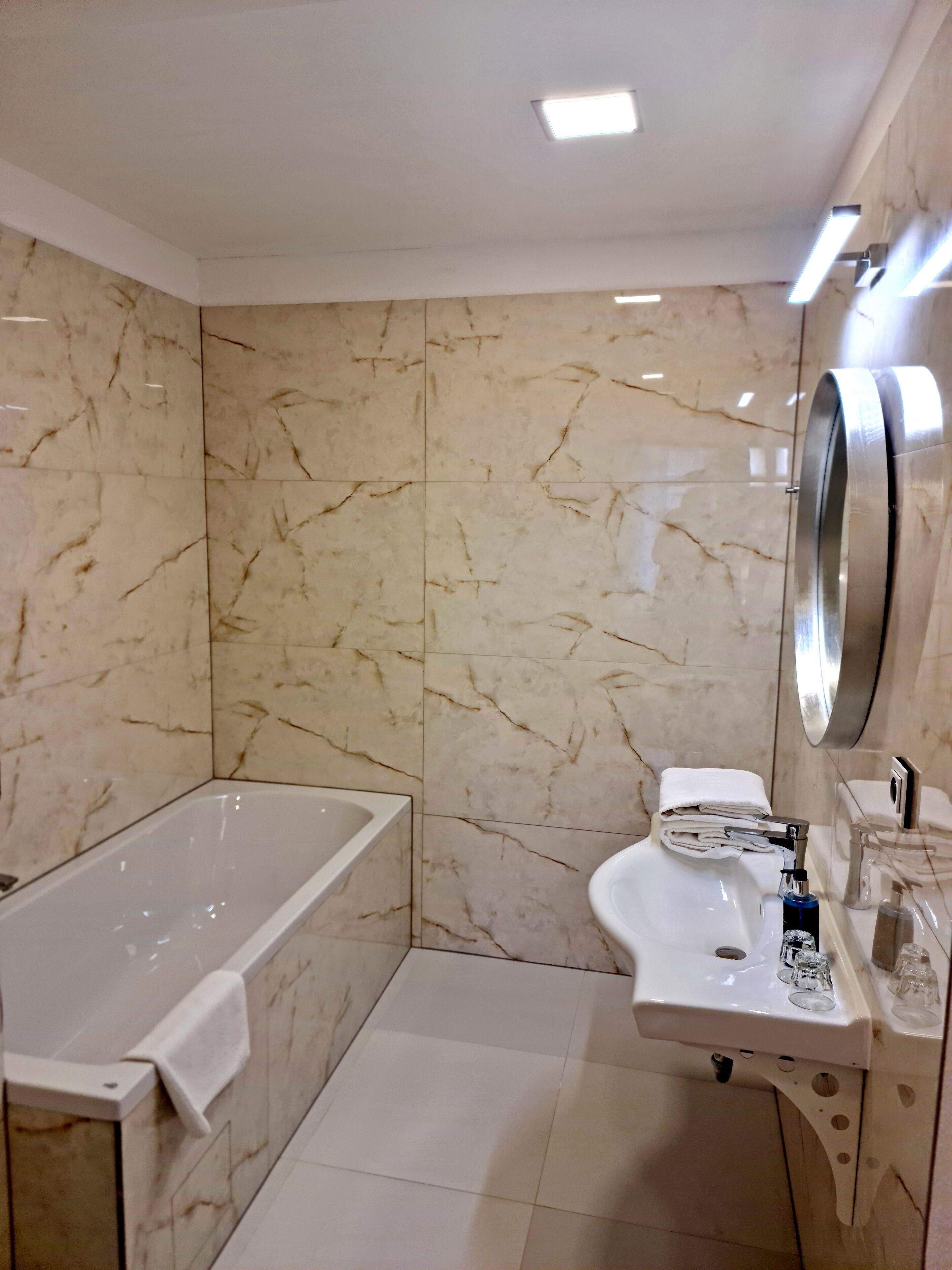 A bathroom with a bathtub, sink, and toilet. The walls are tiled with a marble pattern.