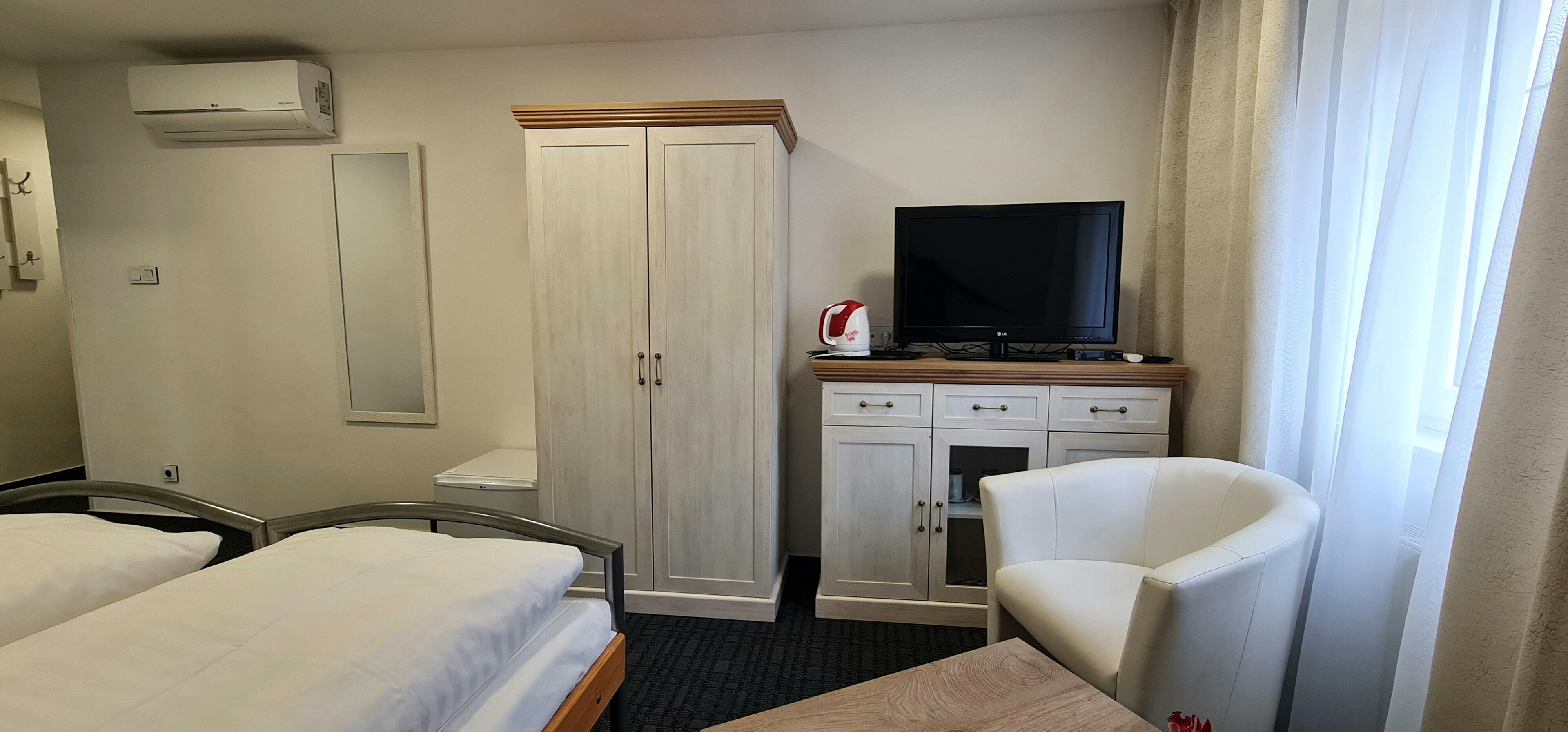 A hotel room with two beds, a wardrobe, a television, a desk, and a chair.