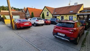 Un estacionamiento con varios autos, un edificio con la leyenda 'Pension' y una pequeña tienda.