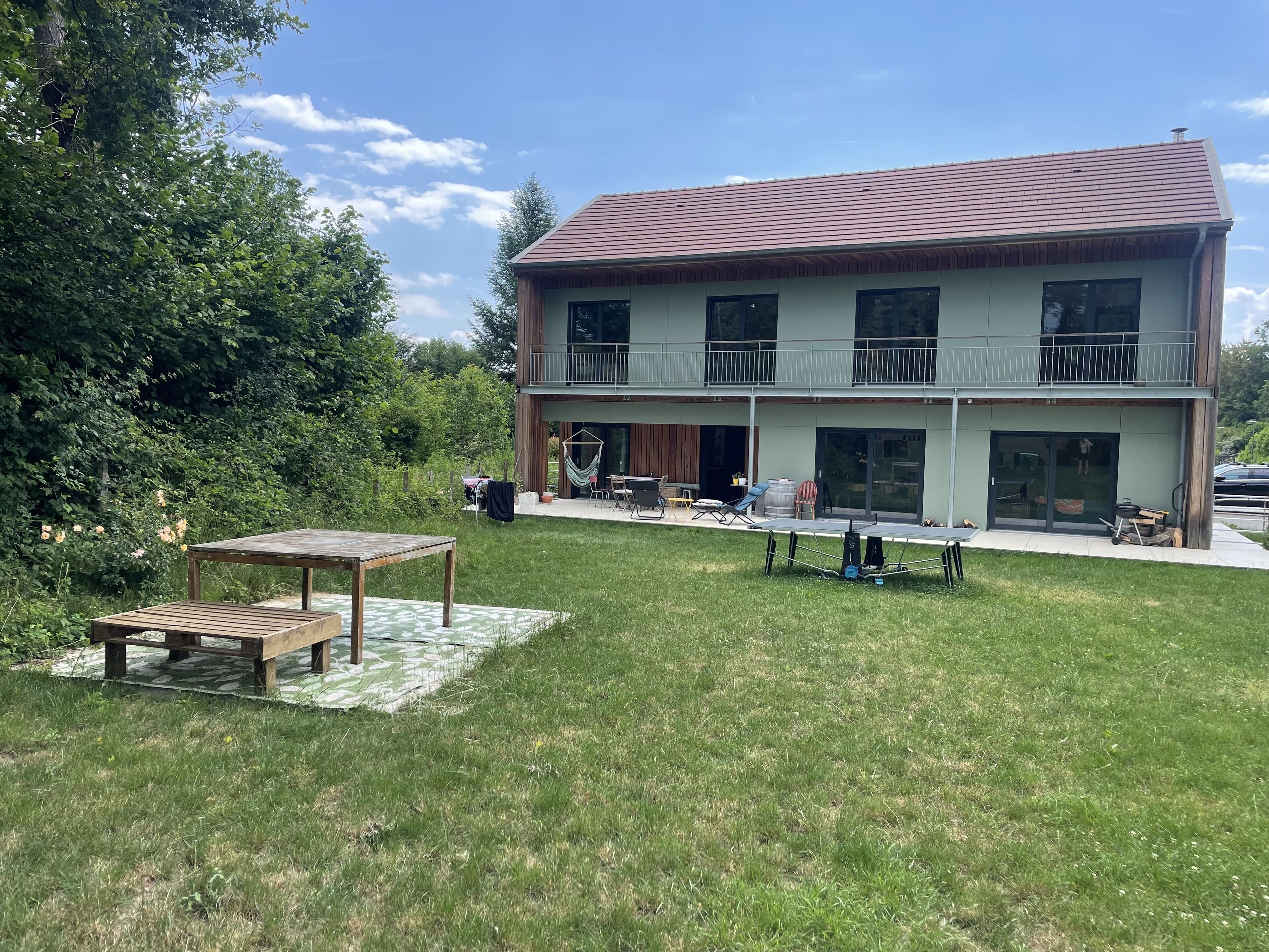 A two-story building with a balcony, a patio area with outdoor furniture, and a grassy lawn.
