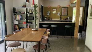 A modern kitchen with a central island, bar stools, and a dining area with a wooden table and chairs. - Maison d’architecte en bois (Chevry)