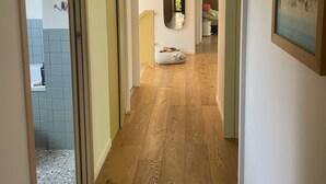 A hallway with wooden flooring, a mirror, and a painting on the wall. - Maison d’architecte en bois (Chevry)