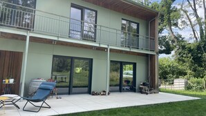 A two-story house with a balcony, large windows, and a patio area with outdoor furniture. - Maison d’architecte en bois (Chevry)