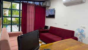 Ein Zimmer mit Schreibtisch, Computer, einem roten Sofa, einem pinken Stuhl und einem Fenster mit roten Vorhängen.