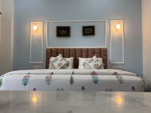 Une chambre à coucher avec un lit, une couvre-lit à motifs floraux, deux lampes fixées au mur et deux tableaux encadrés accrochés au mur.