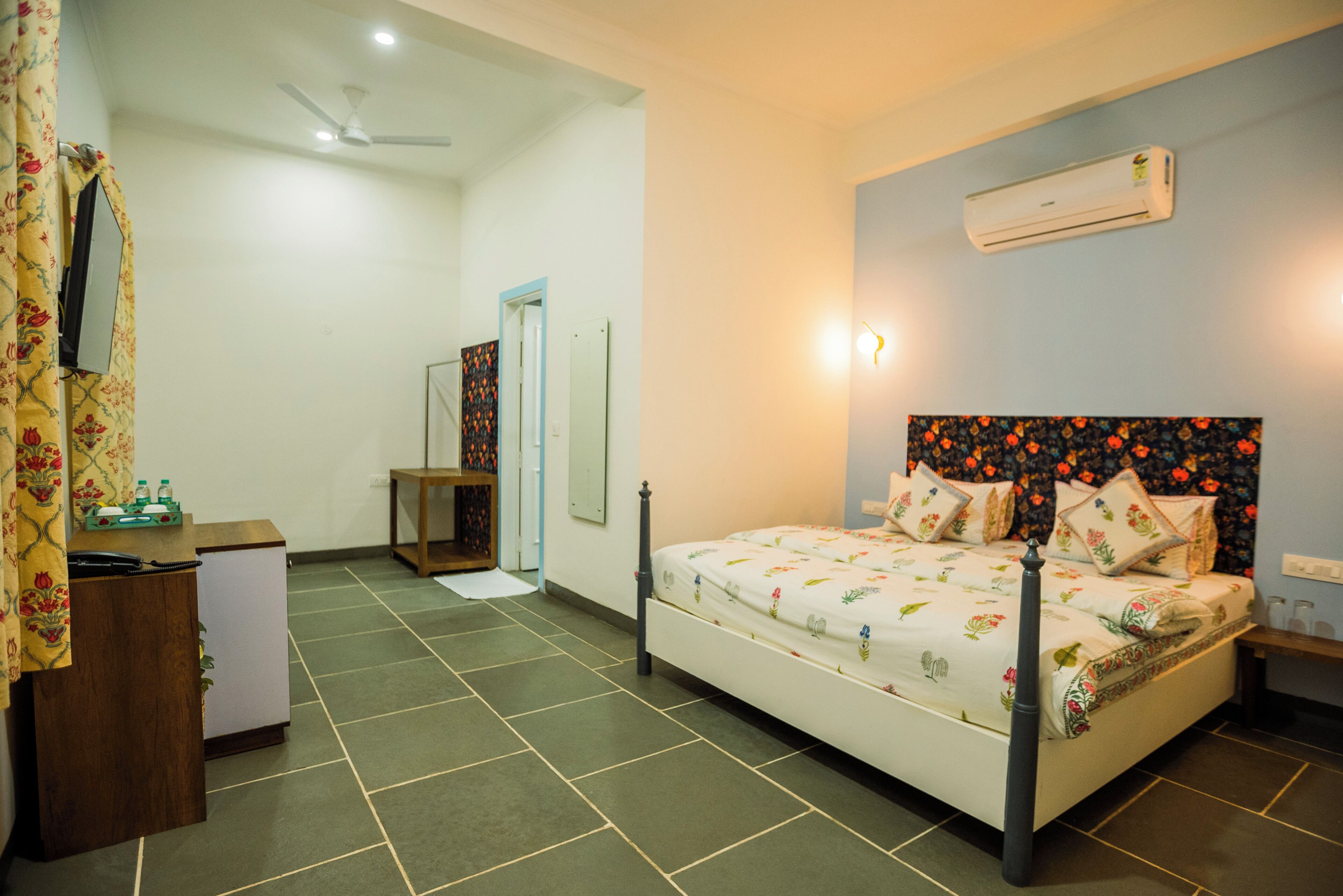 A bedroom with a bed, a desk, a wardrobe, and an air conditioning unit.