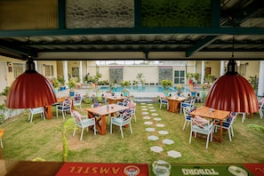 Un espacio de patio al aire libre con baldosas hexagonales, mesas y sillas de madera, y lámparas rojas colgantes.