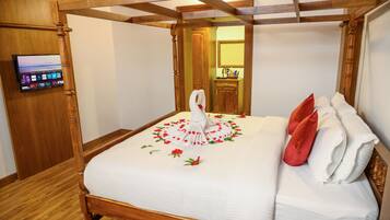 A four-poster bed with a white bedspread and red roses, a wooden floor, and a television on the wall.