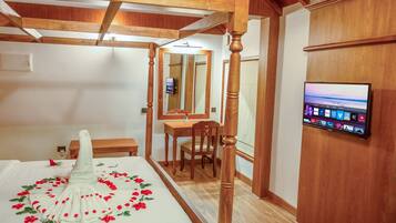 A bedroom with a four-poster bed, a wooden desk, a chair, a television mounted on the wall, and a mirror.