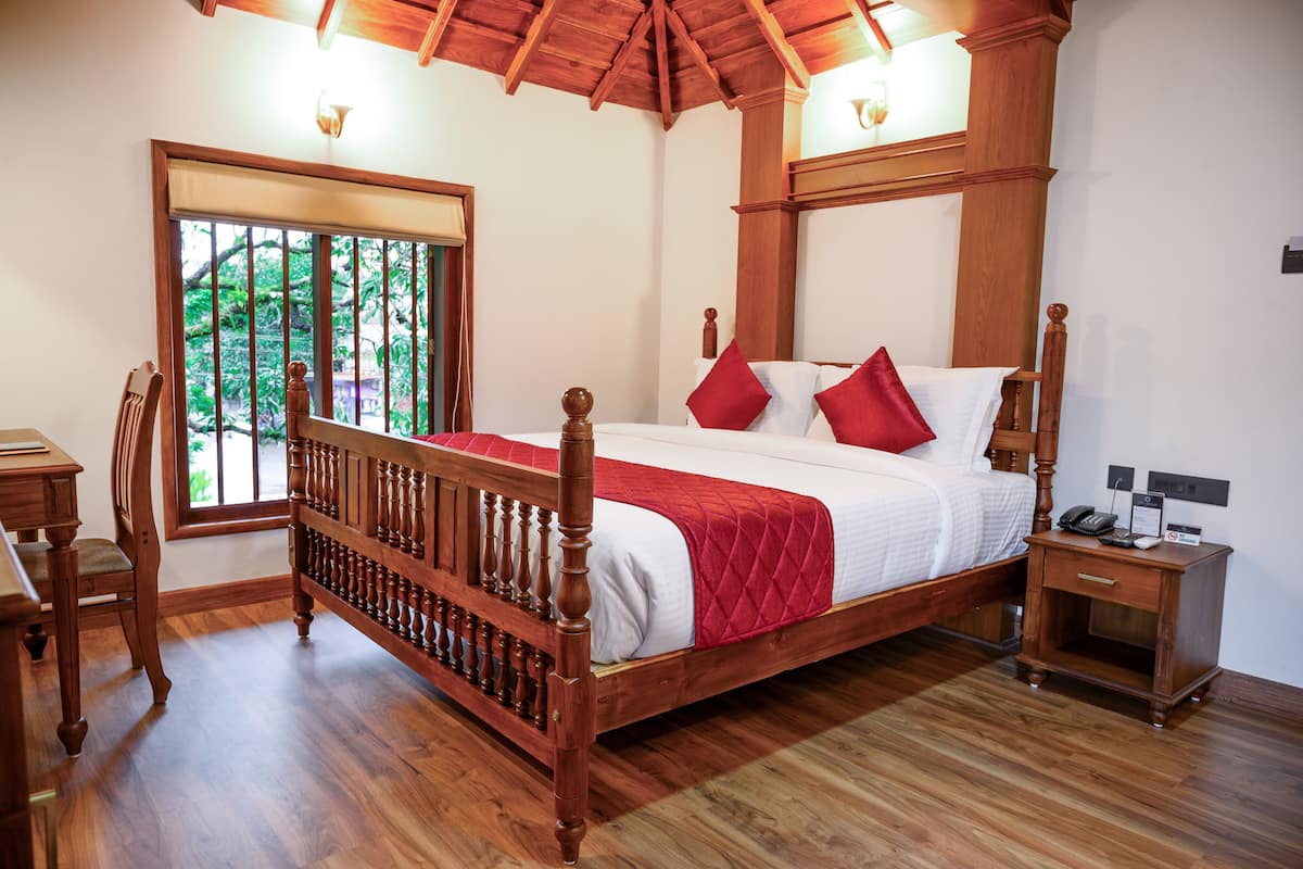 Una cama con dosel de madera, con una colcha roja y blanca, una mesita de noche con un teléfono y un cartel, y una silla de madera.