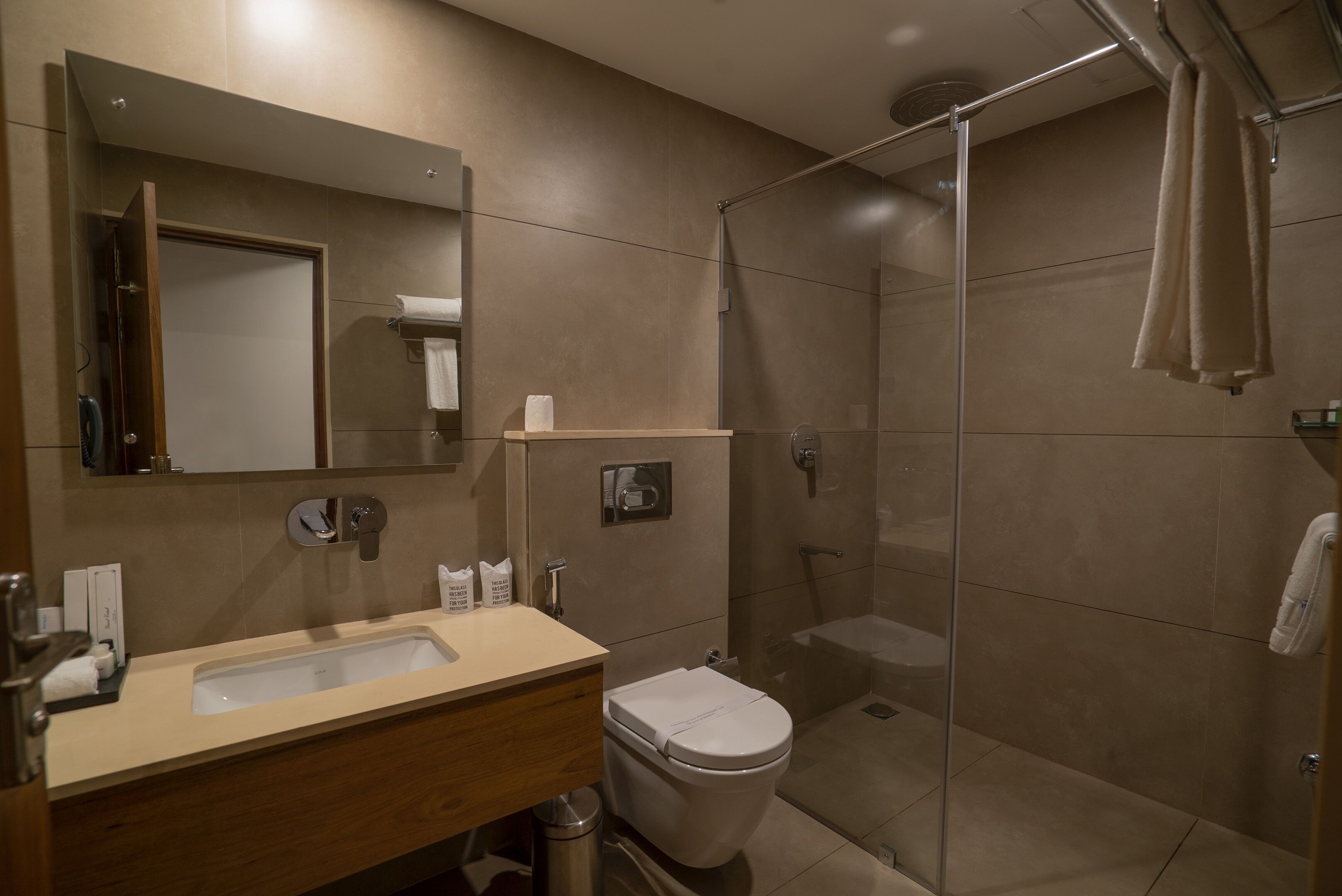 A modern bathroom with a sink, mirror, toilet, and glass-enclosed shower.