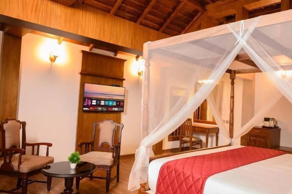 Un dormitorio con una cama con dosel, un televisor montado en la pared y una zona de comedor con sillas y una mesa.