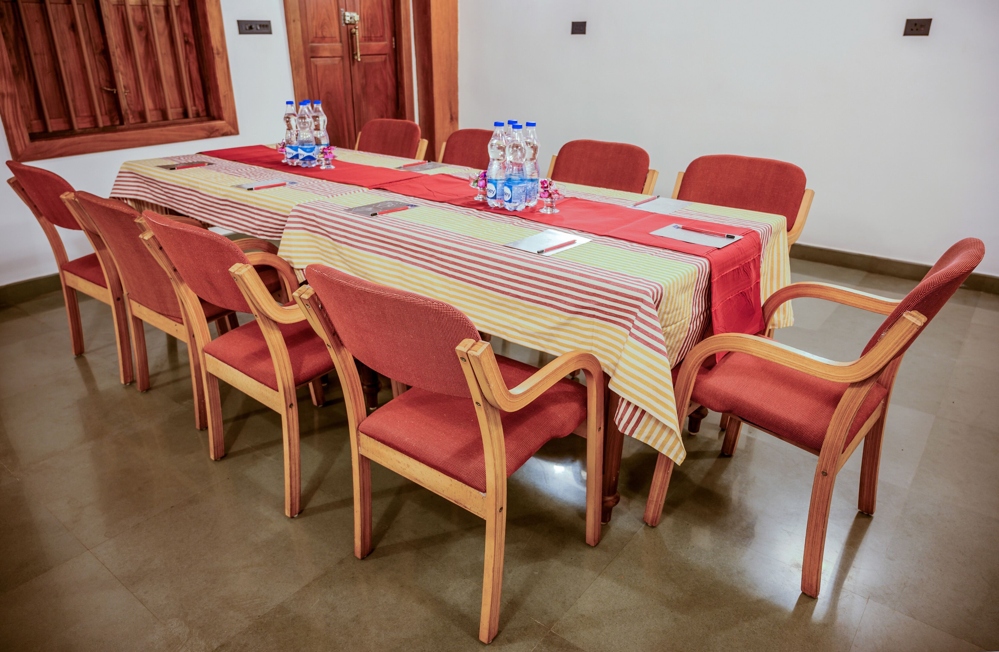 A conference room with a long table, red chairs, and water bottles on the table.