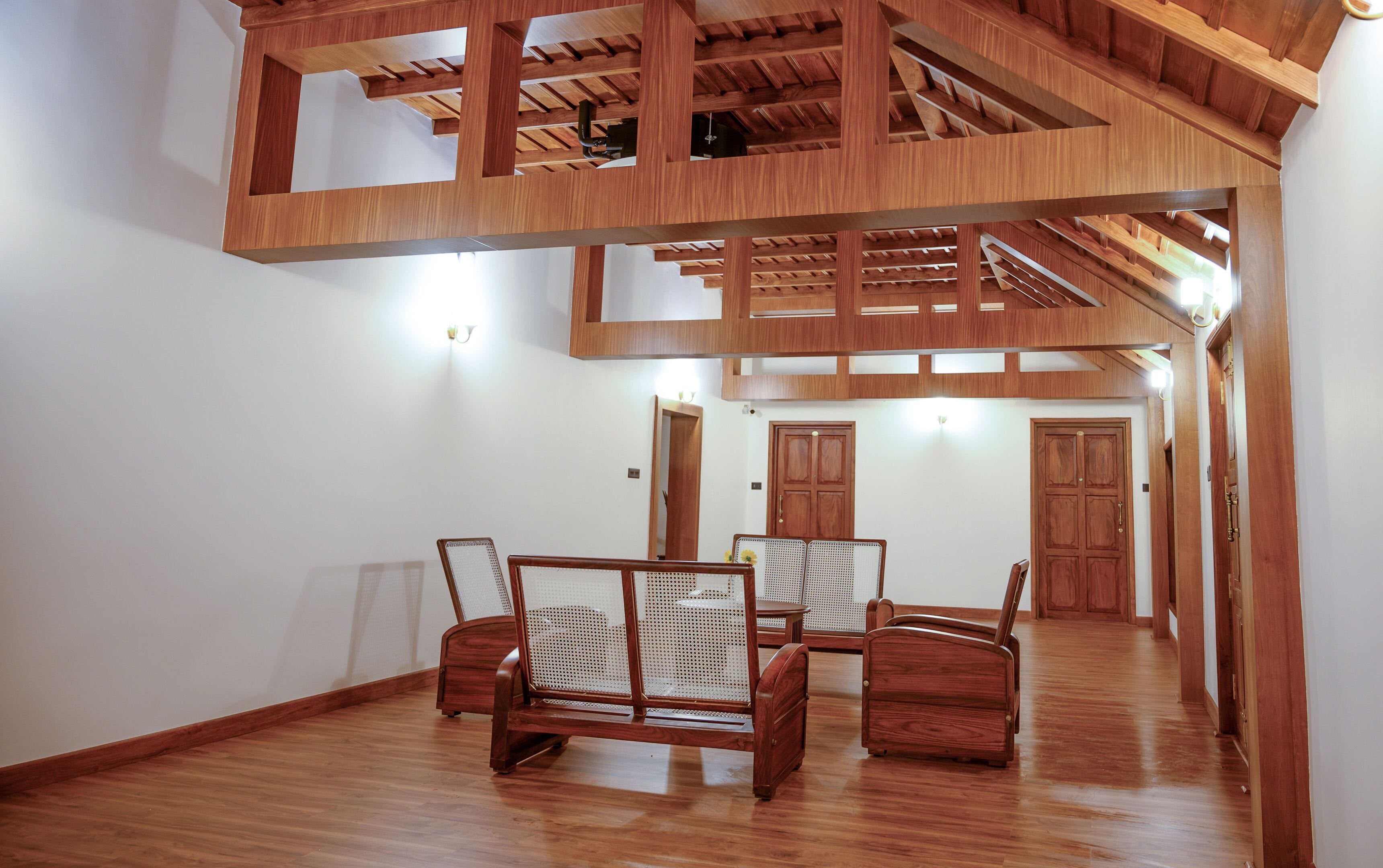 A spacious room with a high ceiling and wooden beams, featuring a central seating area with two chairs and a sofa.