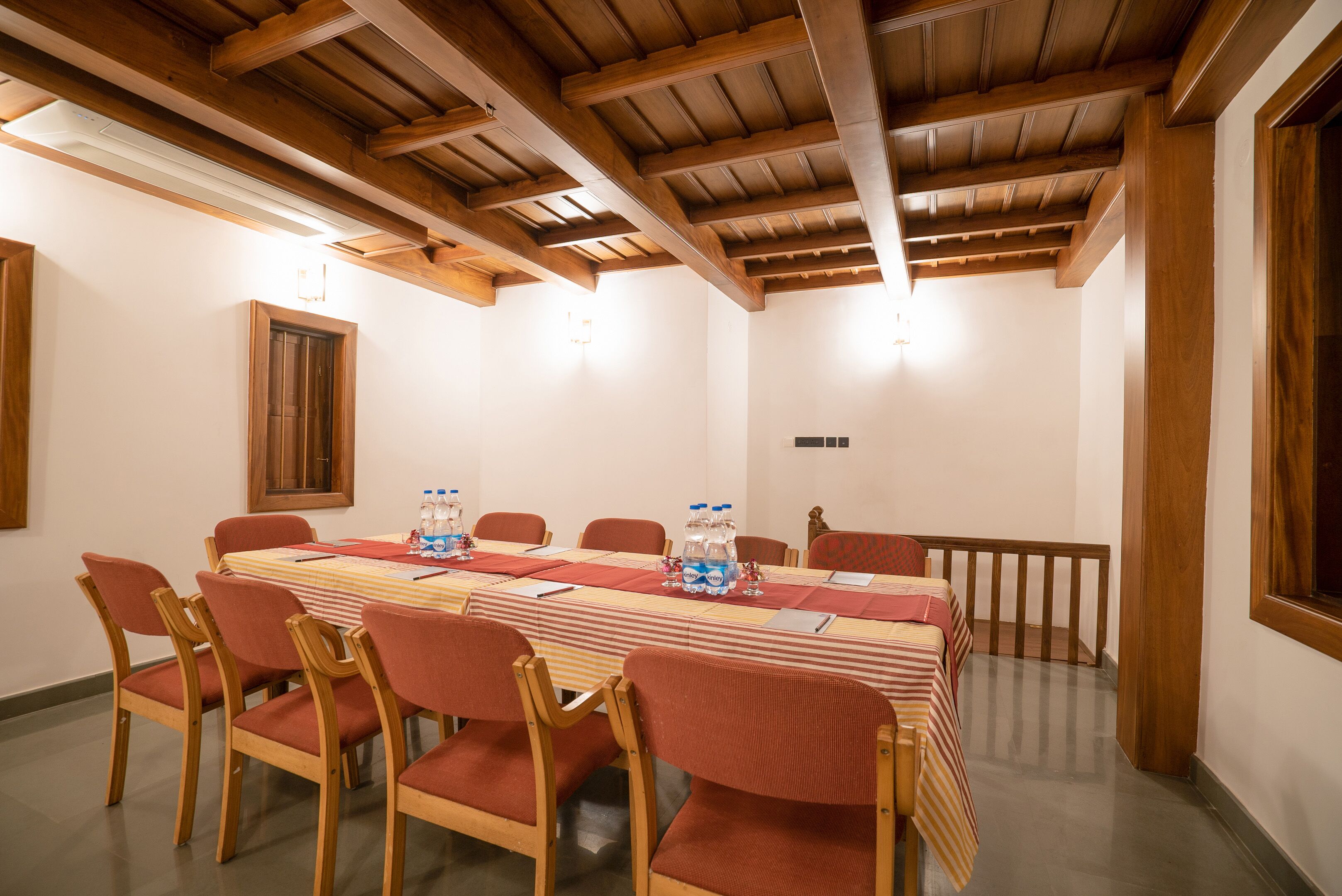 Un salón de conferencias con una larga mesa, sillas rojas y vigas de madera en el techo.