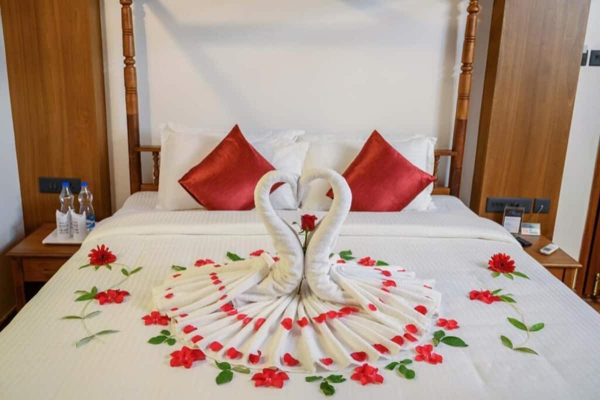 Habitación de hotel con una cama decorada con un diseño de cisne y rosa, almohadas rojas y cabecero de madera.