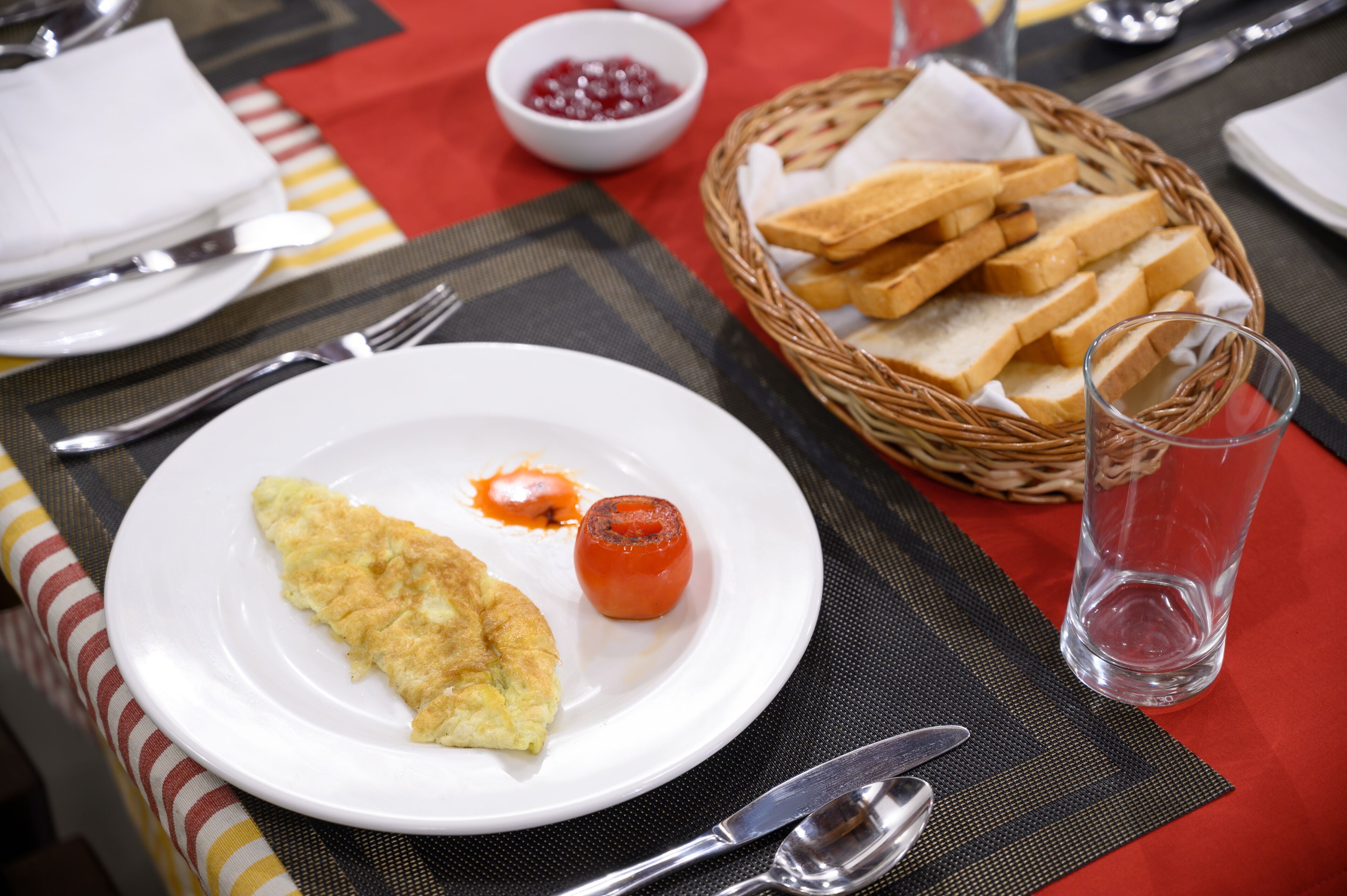 Une table mise pour le petit-déjeuner, avec une assiette de nourriture, un verre d’eau et un panier de pain.