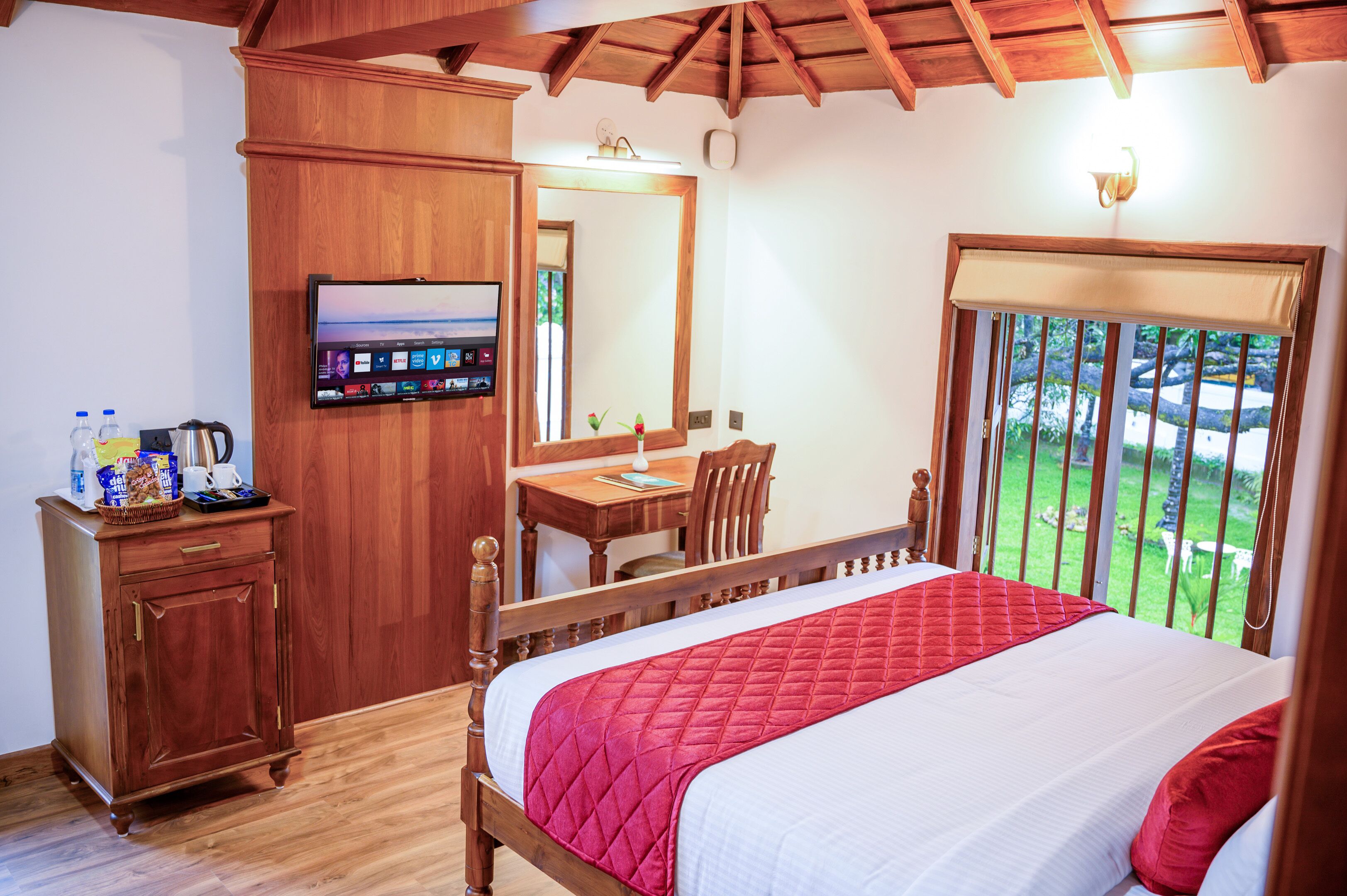A bedroom with a wooden bed, a desk with a chair, a television, and a view of the outdoors.